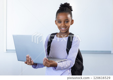 In school classroom, african american girl holding laptop and smiling with backpack In school classroom, african american girl holding laptop and smiling with backpack 120616529