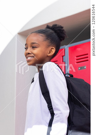 Smiling african american girl with backpack standing near school lockers, ready for class 120616544
