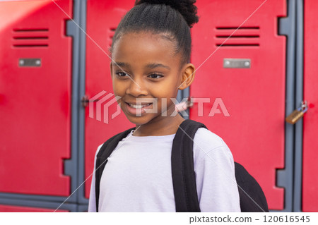 Smiling african american girl with backpack standing in front of red school lockers Smiling african american girl with backpack standing in front of red school lockers 120616545