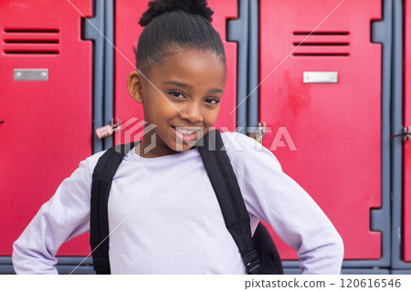 Smiling african american girl with backpack standing in front of red lockers at school Smiling african american girl with backpack standing in front of red lockers at school 120616546