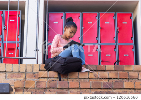 Sitting on steps, african american girl reading tablet in front of school lockers Sitting on steps, african american girl reading tablet in front of school lockers 120616560