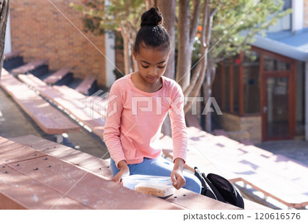 Sitting on bench, african american girl in school opening lunchbox during break Sitting on bench, african american girl in school opening lunchbox during break 120616576