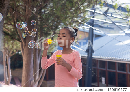 Blowing bubbles, african american girl enjoying outdoor activity at school playground with friends 120616577