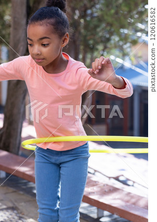 Playing with hula hoop, african american girl enjoying outdoor activity at school playground Playing with hula hoop, african american girl enjoying outdoor activity at school playground 120616582