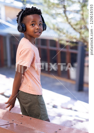 Listening to music with headphones, african american boy walking outside school building 120616593