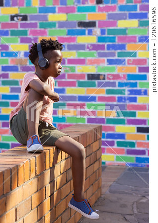 Listening to music with headphones, african american boy sitting on brick wall at school 120616596