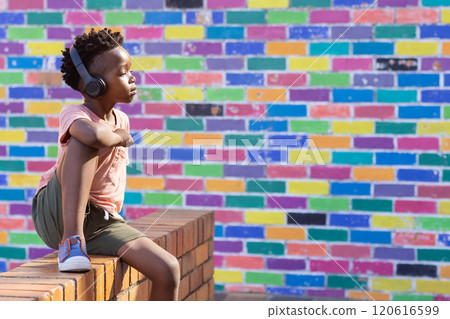Listening to music with headphones, african american boy, brick wall outside school, copy space 120616599