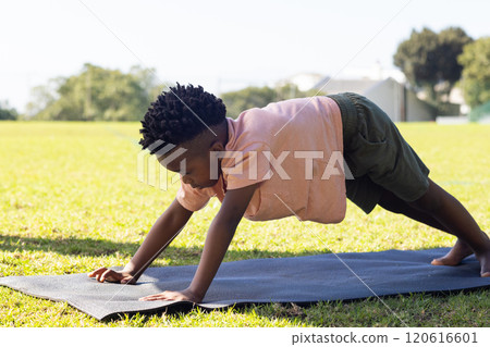 Practicing yoga, african american boy doing plank pose on yoga mat outdoors at school 120616601