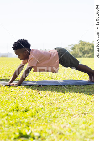 Practicing yoga, african american boy stretching on mat outdoors in school field Practicing yoga, african american boy stretching on mat outdoors in school field 120616604