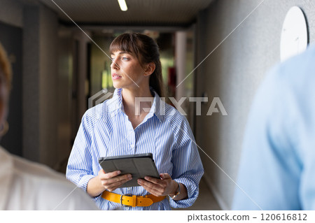 Holding tablet, woman in office hallway looking thoughtful and focused 120616812