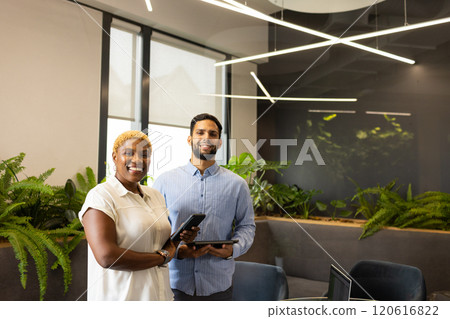 Smiling colleagues holding tablets in modern office with green plants, copy space 120616822