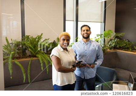Smiling colleagues holding tablets in modern office with indoor plants 120616823