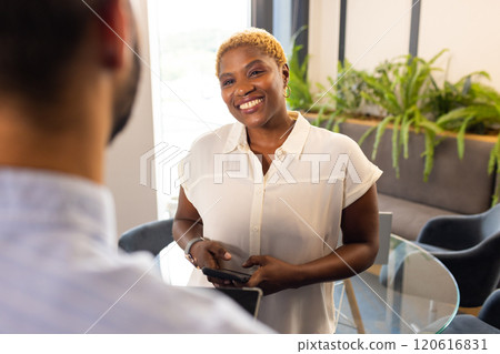 Smiling woman holding smartphone, engaging in conversation with colleague in office Smiling woman holding smartphone, engaging in conversation with colleague in office 120616831