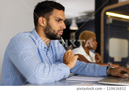 Working in office, african american man holding pen and thinking, woman in background typing Working in office, african american man holding pen and thinking, woman in background typing 120616832