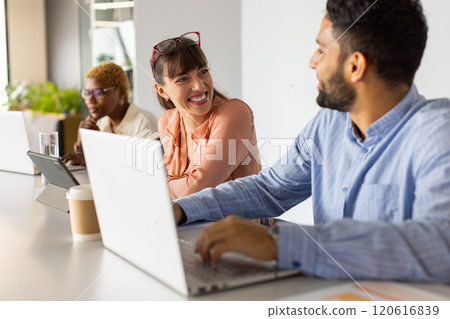 Working in office, colleagues discussing project using laptops and tablet, smiling Working in office, colleagues discussing project using laptops and tablet, smiling 120616839