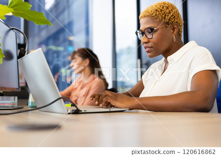 Working on laptop, woman in glasses typing at desk in modern office 120616862