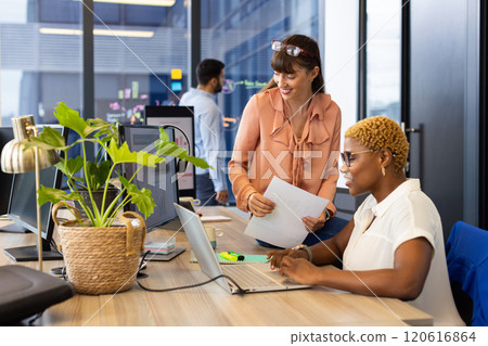 Collaborating at office, two women using laptop and documents discussing project Collaborating at office, two women using laptop and documents discussing project 120616864
