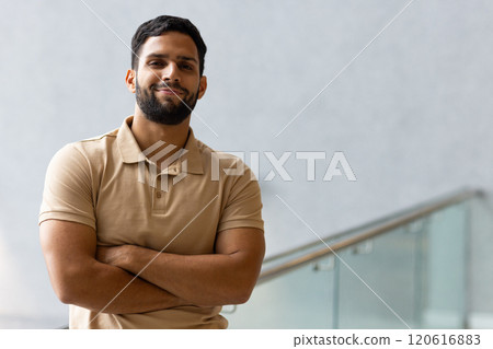 Confident man crossing arms and smiling, standing indoors near glass railing, copy space Confident man crossing arms and smiling, standing indoors near glass railing, copy space 120616883