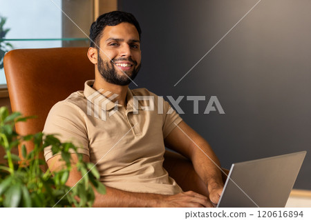 Smiling man using laptop while sitting in comfortable chair at home Smiling man using laptop while sitting in comfortable chair at home 120616894