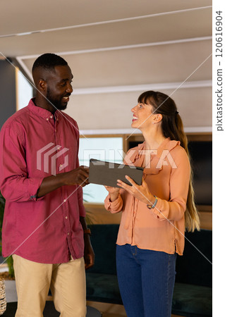 Discussing project details, colleagues using tablet and smiling in modern office 120616904