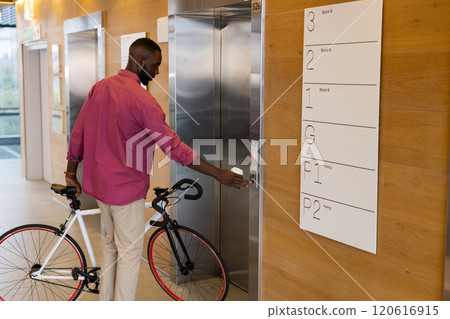 Man with bicycle pressing elevator button in modern office building 120616915