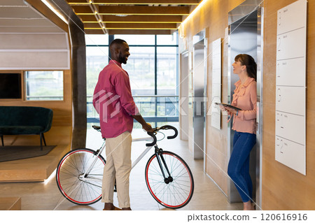 Man with bicycle talking to woman holding tablet in modern office hallway Man with bicycle talking to woman holding tablet in modern office hallway 120616916