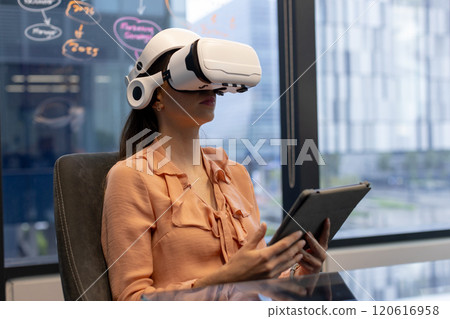 Using VR headset and holding tablet, woman working in modern office 120616958