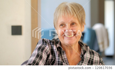Cheerful elderly woman with a warm smile, wearing a plaid shirt, enjoying a pleasant moment indoors. Cheerful elderly woman with a warm smile, wearing a plaid shirt, enjoying a pleasant moment indoors. 120617036