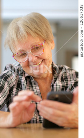 Senior woman smiling as she uses her smartphone, enjoying a moment of technology engagement indoors. 120617038
