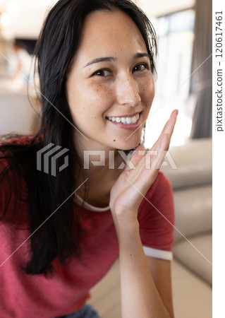 On video call, smiling woman in red shirt posing indoors, at home 120617461
