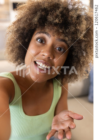 On video call, smiling woman in green top gesturing while talking, at home 120617462