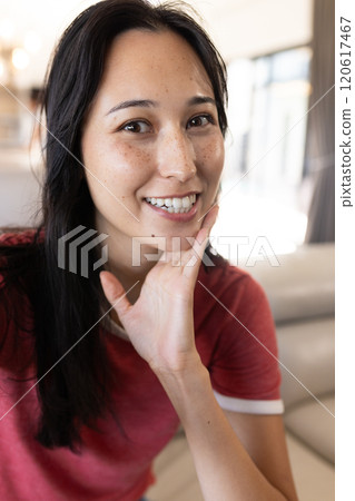 On video call, smiling woman in red shirt posing indoors, at home 120617467