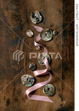 Various handmade flat ceramic beads on pink ribbon. Hobby, jewelry assembly, DIY jewelry. Workshop idea. Dark wooden background, top view. 120617492
