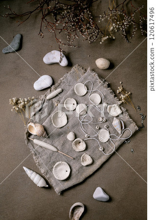 Ceramic workshop idea: handcrafted beads from clay or porcelain. Flat beads of raw white porcelain on rough fabric. Small white flowers, jewelry findings, sea shells. Dark background, top view. Ceramic workshop idea: handcrafted beads from clay or porcelain. Flat beads of raw white porcelain on rough fabric. Small white flowers, jewelry findings, sea shells. Dark background, top view. 120617496
