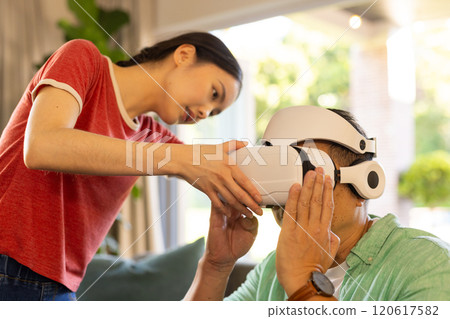 Helping father adjust VR headset, daughter ensuring proper fit and comfort Helping father adjust VR headset, daughter ensuring proper fit and comfort 120617582