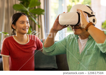 Using VR headset, father exploring virtual reality while daughter smiling nearby 120617584