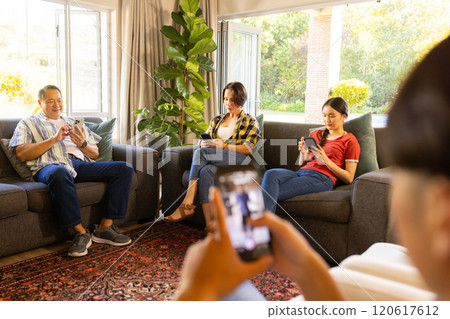 Using smartphones, family sitting on couches in living room, relaxing together 120617612