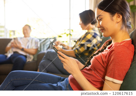 Using smartphones, family members relaxing on couch in living room together 120617615