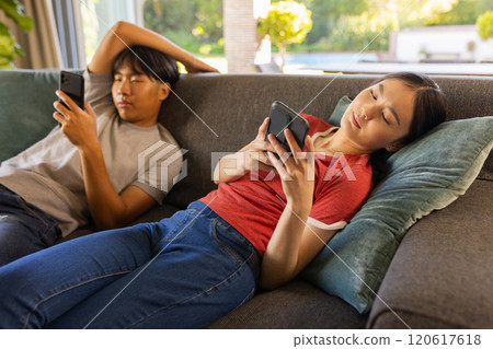 Relaxing on couch, asian brother and sister using smartphones, enjoying leisure time at home 120617618