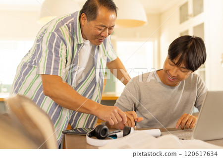 Asian father helping son with homework, using laptop and writing in notebook 120617634