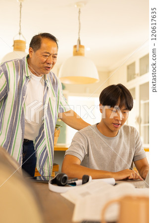 Asian father and son studying together at home, using laptop and books 120617635