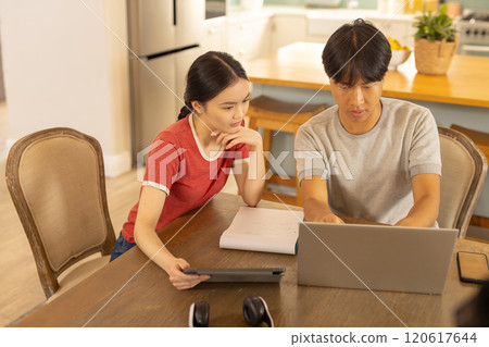 Working from home, asian brother and sister using laptop and tablet at kitchen table 120617644