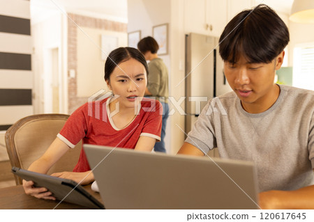 Using laptop and tablet, young asian brother and sister discussing something in kitchen 120617645