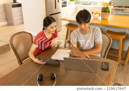 Working from home, asian brother and sister using laptop and tablet at kitchen table 120617647