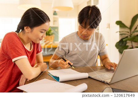 Studying together, young asian brother and sister using laptop and writing notes 120617649