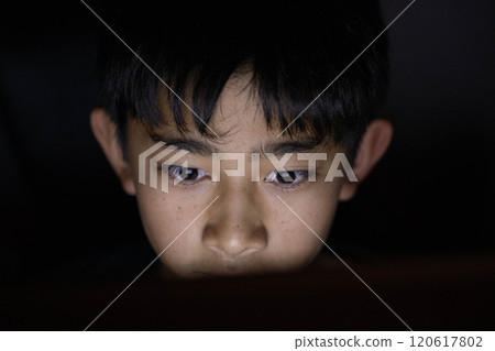 Boy looking at a computer in the middle of the night 120617802