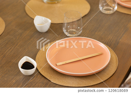 Chopsticks on pink plate with soy sauce and glass on dining table Chopsticks on pink plate with soy sauce and glass on dining table 120618089