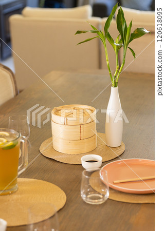 Dining table with bamboo steamer, vase with bamboo plant, and lemonade pitcher 120618095