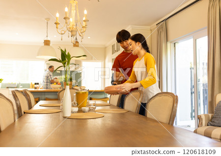 Setting table for family meal, young asian brother and sister arranging dishes in dining room Setting table for family meal, young asian brother and sister arranging dishes in dining room 120618109