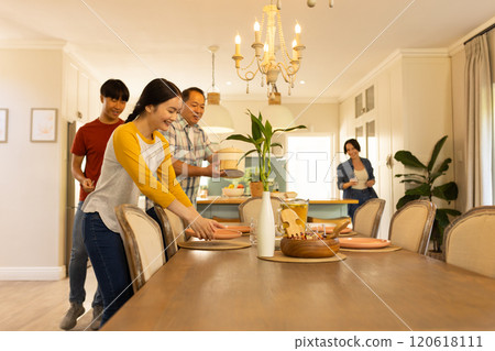 Setting dining table, multiracial family preparing for meal together in cozy home dining room Setting dining table, multiracial family preparing for meal together in cozy home dining room 120618111